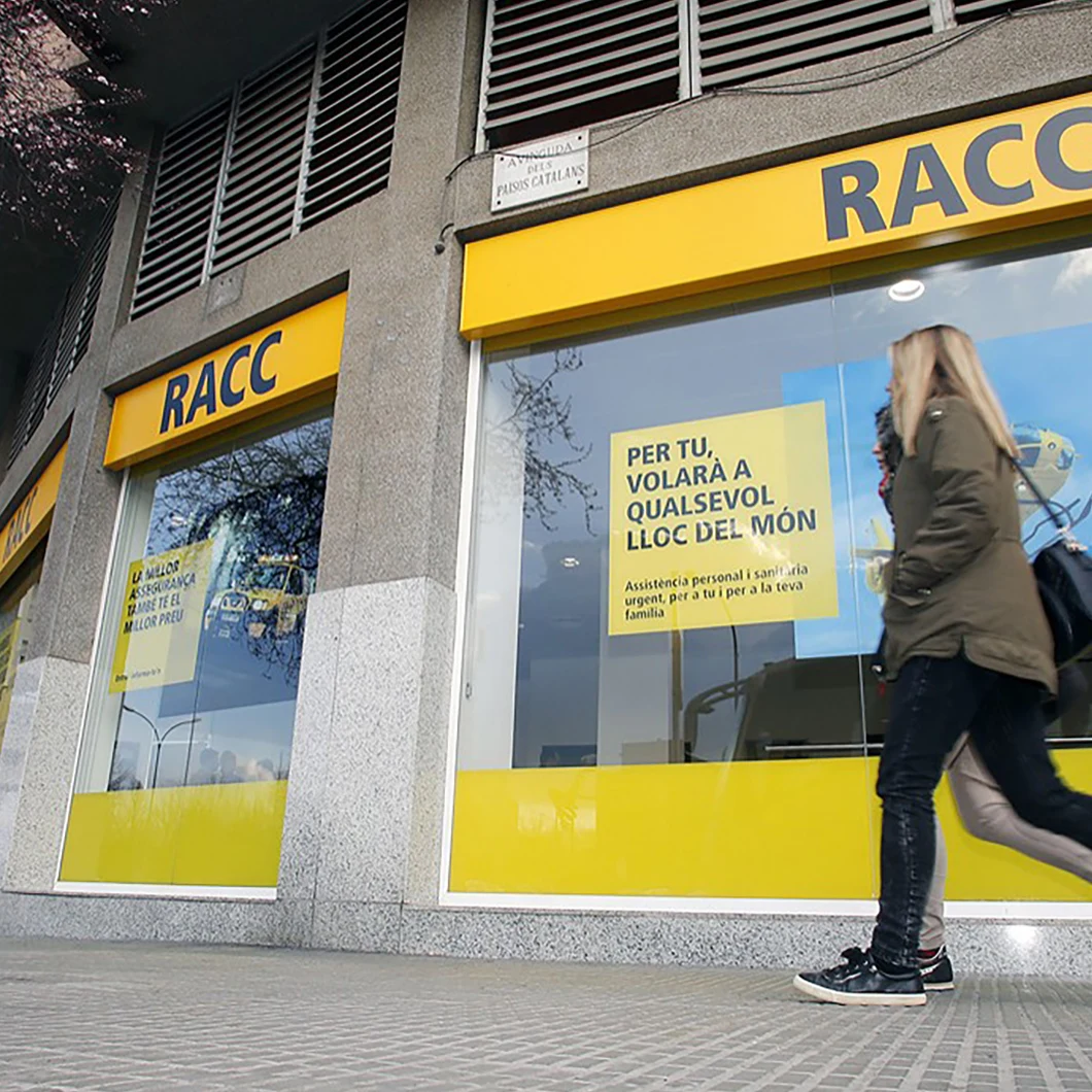 Pedestrian walking past a RACC storefront with yellow window graphics promoting personal and medical assistance abroad