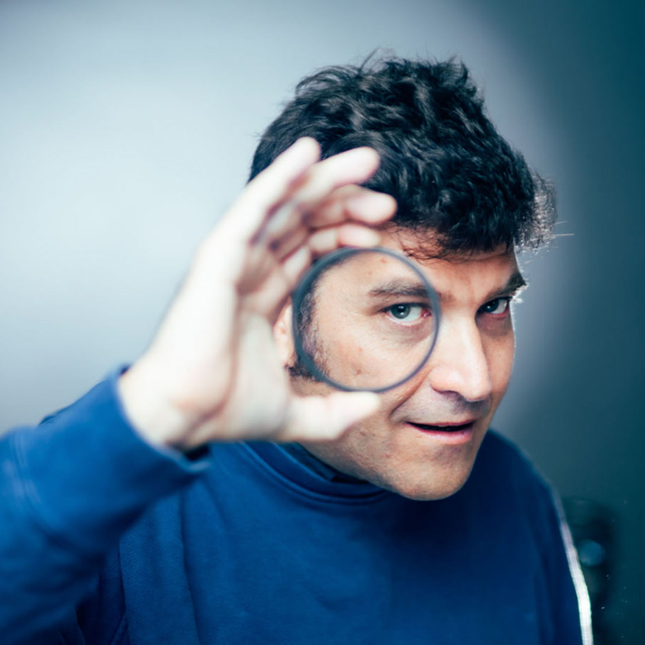 Portrait of Julián Waisbord looking through a circular lens aligned with his eye — a direct reference to the logo's optical concept.